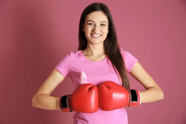 Jonge vrouw in roze t-shirt en bokshandschoenen op kleur achtergrond. Borst kanker bewustzijn concept — Stockfoto