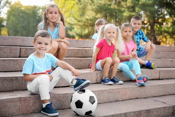 Lindos niños pequeños con pelota sentados en las escaleras en el parque de la ciudad — Foto de Stock
