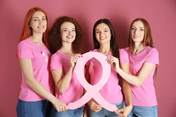 Mulheres jovens em camisetas rosa segurando fita consciência câncer de mama no fundo de cor — Fotografia de Stock