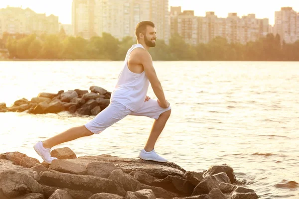 Handsome young man exercising on river bank — Stock Photo, Image