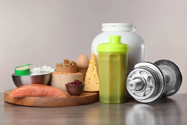 Composition with protein shake, food and dumbbell on table