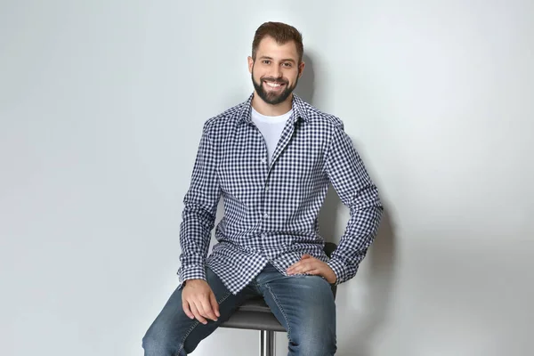 Handsome man sitting against light background — Stock Photo, Image