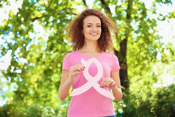 Mujer joven en camiseta rosa que sostiene la cinta de conciencia del cáncer de mama al aire libre — Foto de Stock