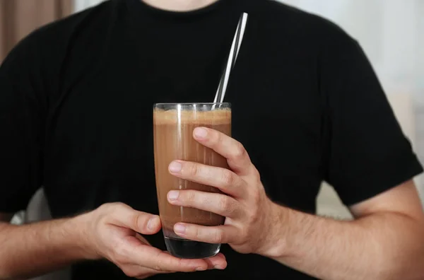 Человек держит стакан с протеиновым коктейлем в помещении — стоковое фото