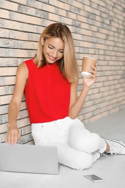 Jolie femme avec ordinateur portable moderne assis près du mur de briques — Photo
