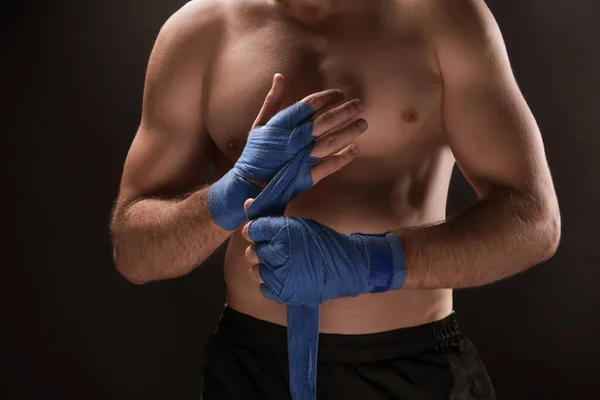 Male boxer applying wrist wraps on dark background