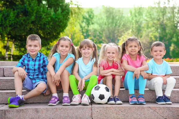 Crianças pequenas bonitos com bola sentada em escadas no parque da cidade — Fotografia de Stock
