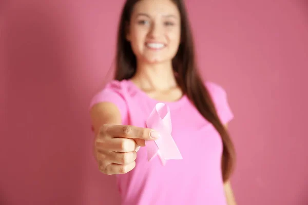 Young woman in pink t-shirt holding ribbon on color background. Breast cancer awareness concept — Stock Photo, Image