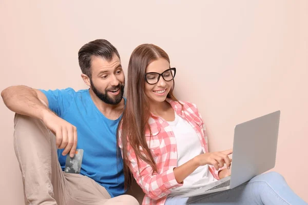 Jeune couple avec ordinateur portable et carte de crédit sur fond de couleur. Concept de magasinage Internet — Photo