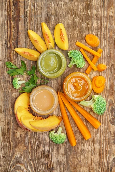 Frascos con diferentes alimentos para bebés en mesa de madera — Foto de Stock