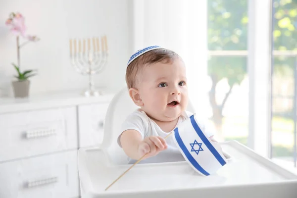 Симпатичный ребенок в киппе с флагом Израиля, сидящий на высоком стульчике дома — стоковое фото