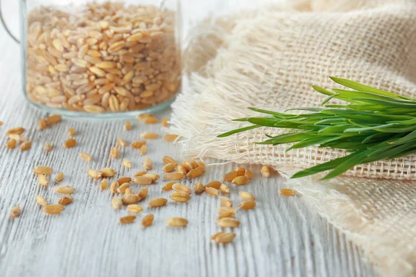Verspreide zaden en tarwe gras op houten tafel — Stockfoto