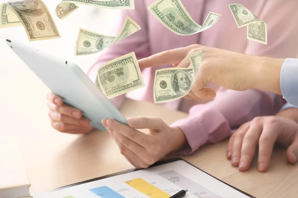 Geld fliegt aus dem Tablet, während die Leute es am Tisch im Büro verwenden — Stockfoto