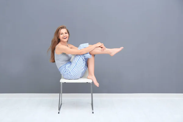 Junge schöne Frau sitzt auf Stuhl in der Nähe der grauen Wand — Stockfoto