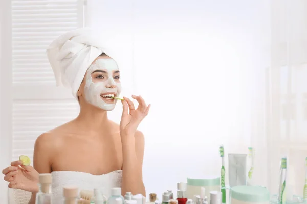 Jeune femme avec masque facial et tranches de concombre dans la salle de bain — Photo