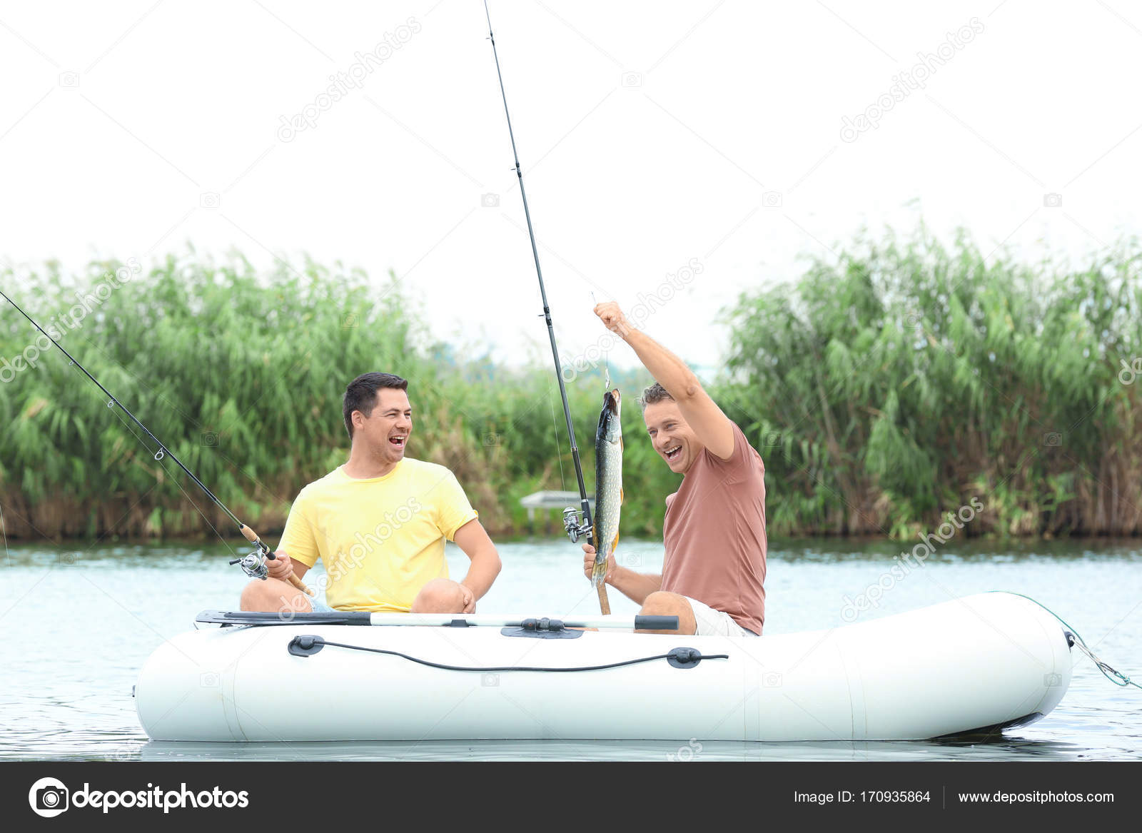 Two men fishing from inflatable boat on river Stock Photo by