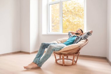 Genç adam evde pencere yakınındaki koltuk dinlenme