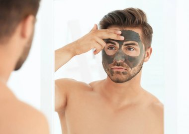 Genç adam banyoda yüzünde kozmetik maskesi uygulama