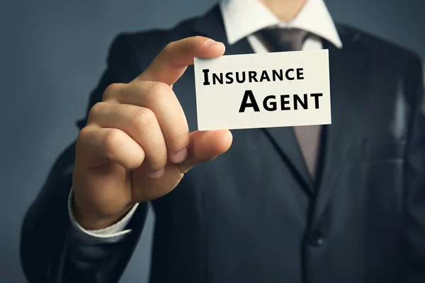 Podnikatel, drží vizitka pojišťovacího agenta na tmavém pozadí — Stock fotografie