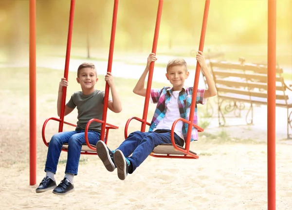 Lindos niños pequeños en columpios en el parque — Foto de Stock