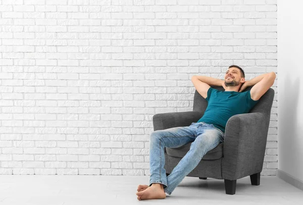 Young man resting in armchair against brick wall background — Stock Photo, Image