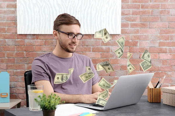 L'argent s'envole hors de l'ordinateur portable tandis que l'homme l'utilise à la table au bureau — Photo