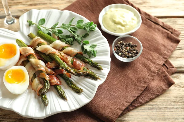 Piatto con asparagi avvolti nella pancetta sul tavolo — Foto Stock