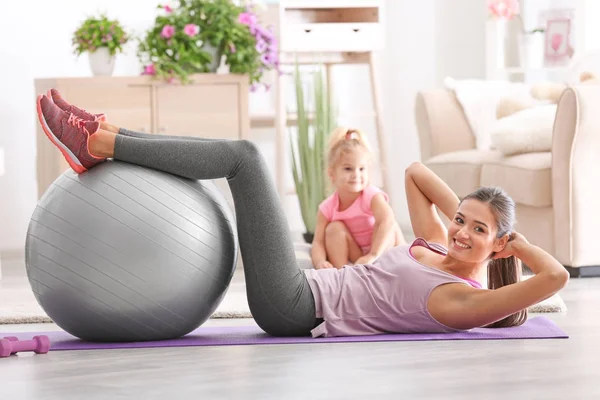 Schöne junge Frau beim Training, während ihre kleine Tochter zu Hause spielt — Stockfoto