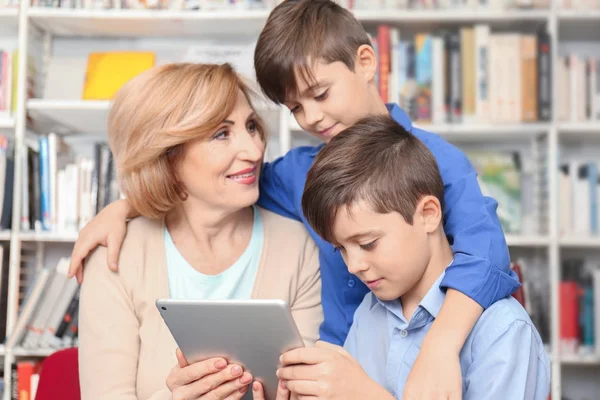 Maestra y niños con tableta en la biblioteca escolar — Foto de Stock
