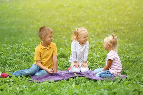 Leuke lieve kinderen zitten op gazon in groen park — Stockfoto