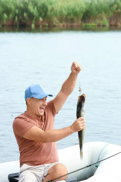 Hombre con pescado recién capturado en bote inflable a orillas del río — Foto de Stock