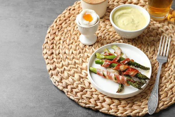 Plate with bacon wrapped asparagus on wicker mat — Stock Photo, Image