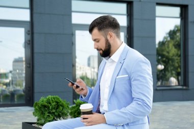 Cep telefonu ve fincan kahve açık havada yakışıklı başarılı iş adamı