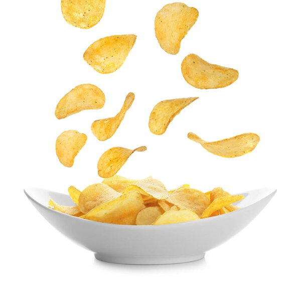 Tasty potato chips falling onto plate 