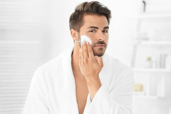 Hombre joven aplicando crema facial en el baño — Foto de Stock