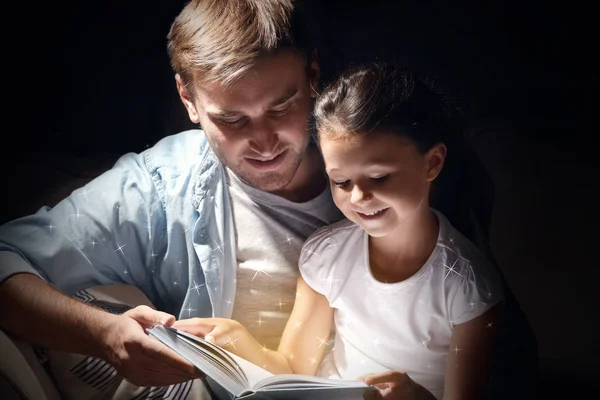 Far med dotter läsa bok på mörk bakgrund — Stockfoto