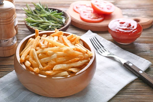 Tigela com deliciosas batatas fritas na mesa de madeira — Fotografia de Stock