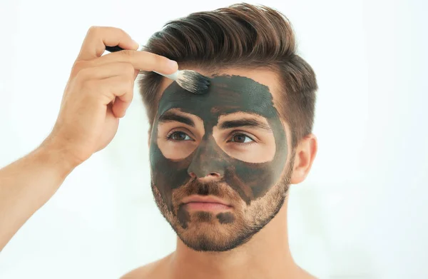 Young man applying cosmetic mask on his face in bathroom — Stock Photo, Image
