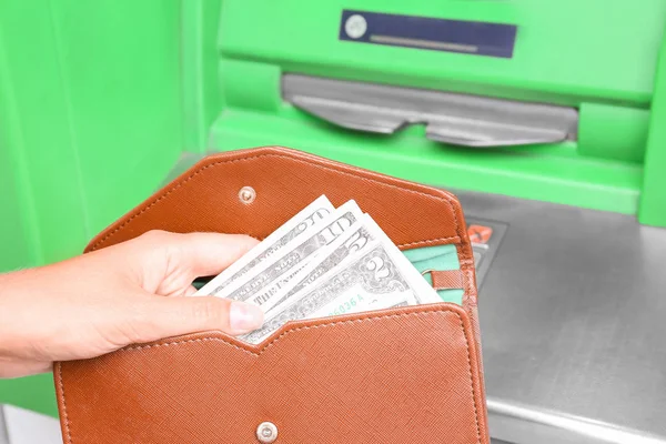 Woman with wallet and money near cash machine, closeup