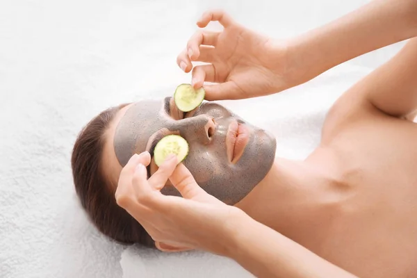 Jonge vrouw met gezichts masker en komkommer plakjes in spa salon — Stockfoto