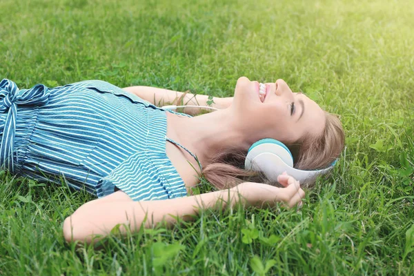 Rahatlatıcı ve açık havada yeşil çim üzerinde yalan sırasında kulaklık müzik dinlemek genç güzel kadın — Stok fotoğraf