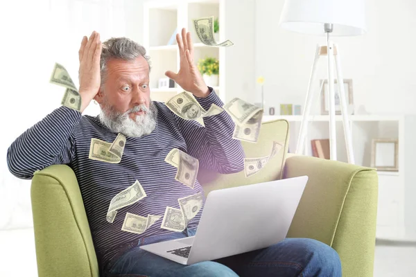 L'argent s'envole hors de l'ordinateur portable tandis que l'homme âgé l'utilise à la maison — Photo