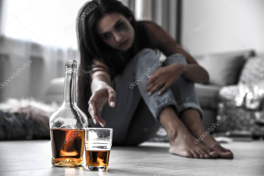 Drunk woman reaching after glass and bottle of alcohol drink on floor