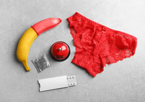 Banana, preservativo, pílulas, sino e calcinha em fundo cinza — Fotografia de Stock