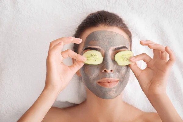 Jovem com máscara facial e fatias de pepino no salão de spa — Fotografia de Stock