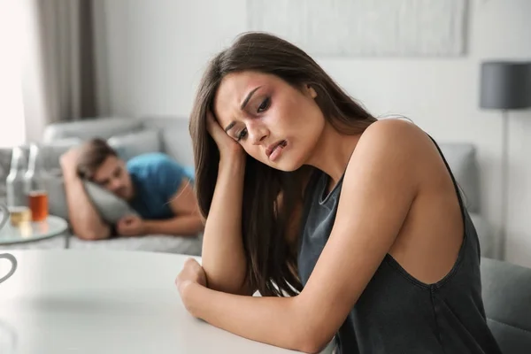 Battered woman and drunk man on sofa at home — Stock Photo, Image