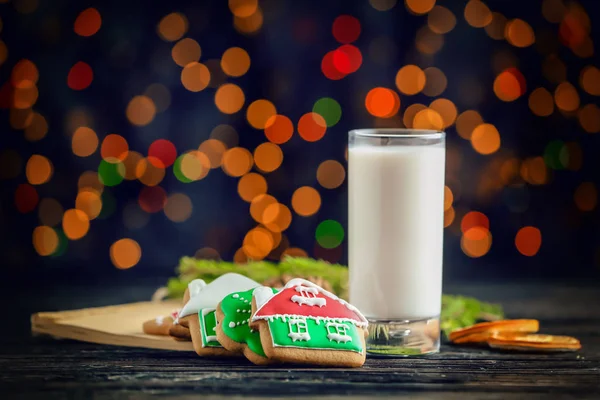 Deliciosos biscoitos e vidro com leite na mesa contra luzes desfocadas — Fotografia de Stock