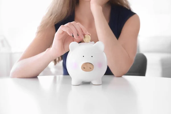 Jonge vrouw munt ingebruikneming piggy bank aan tafel — Stockfoto