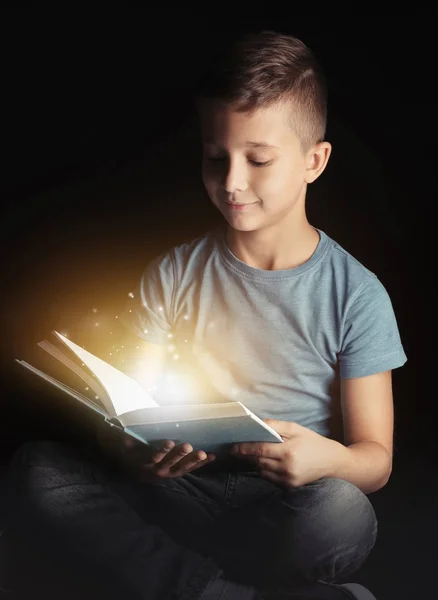 Schattige kleine jongen lezen boek op zwarte achtergrond — Stockfoto