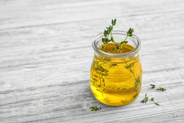 Öl mit Thymian im Glas auf hellem Holzhintergrund — Stockfoto